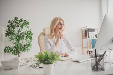 A mature female doctor is seated at her desk in a hospital office, focusing on patient care and consultation, reflecting professionalism and dedication to medical practice. clipart