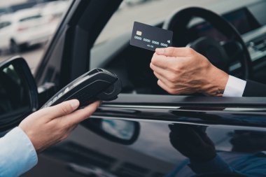 Mature businessman in formal suit makes a contactless payment from his car in a city parking area, showcasing modern technology and convenience. clipart