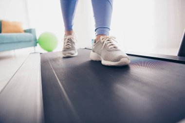 Focus on athletic shoes as a woman jogs on a treadmill in a well-lit, stylish home setting. Perfect for fitness enthusiasts. clipart