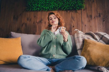 Photo of doubtful unsure woman dressed green cardigan choosing medicines indoors house apartment room. clipart