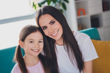 Photo of positive adorable daughter with mom embracing enjoying time together indoors apartment room. clipart