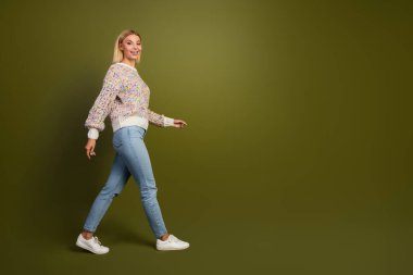 A cheerful young woman in a knit sweater and jeans confidently walks against a khaki background, embodying fashion, style, and positive energy. clipart