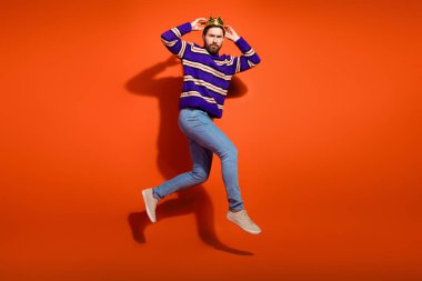 Full length photo of handsome young guy touch crown running jump dressed stylish striped purple garment isolated on orange color background. clipart