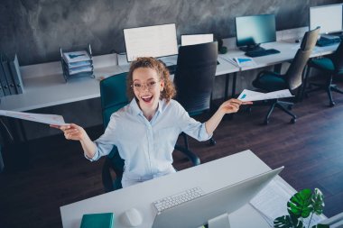 A young female professional celebrating success while holding documents in a modern office setting, conveying achievement and joy. clipart