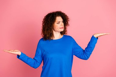 A young woman with curly red hair in a blue sweatshirt gestures in confusion. The vivid pink background adds contrast, capturing expressions of curiosity or decision-making. clipart