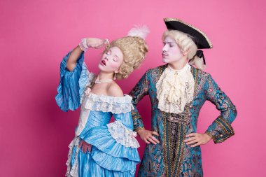 A couple dressed in baroque-style costumes stands in front of a pink backdrop. Their detailed outfits reflect historical elegance and theatrical flair, perfect for a themed costume party. clipart