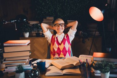 A student sits in a cozy, book-filled setting, wearing a distinctive argyle vest and glasses, embodying a studious lifestyle and casual comfort of home learning and leisure during evening hours. clipart