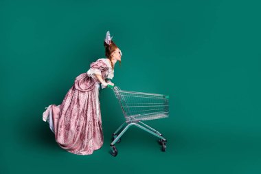 Depiction of a young woman dressed in antique aristocratic style with a pink dress, merging the past and modern life with a shopping cart, on green background. clipart