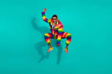 Energetic young man wearing a colorful striped suit leaping joyfully in front of a teal backdrop. A representation of self-expression, individuality, and celebration. clipart