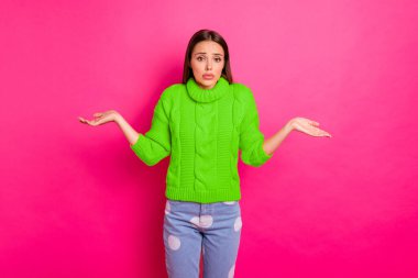 Portrait of worried youth shrugging her shoulders wearing knitted sweater isolated over bright background. clipart