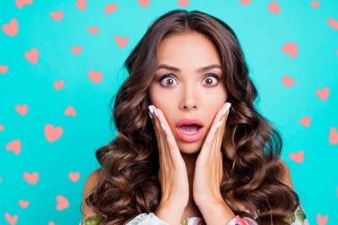 Close up portrait of curly brunette with wow face hold palms on cheeks look at camera with wide open eyes and mouth isolated on bright teal background clipart