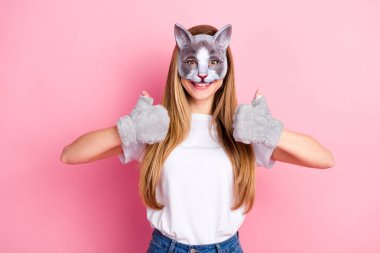 A young woman with long brown hair wearing a cat mask, gray gloves, and a white t-shirt posing and giving thumbs up on a vibrant pink background. clipart