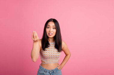 A joyful young woman stands against a pink background, wearing a stylish top and jeans, gesturing playfully. Her cheerful expression reflects a fun, trendy, and leisurely lifestyle. clipart