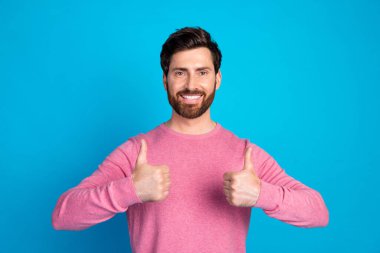 Bearded man in a casual pink sweater showing thumbs up gesture, representing positivity and approval with a bright blue backdrop. clipart