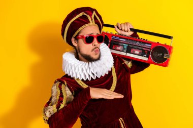 A young male dressed in an ornate medieval noble costume with a ruffled collar, holding a red radio on a bright yellow background, creating a humorous retro and modern contrast. clipart