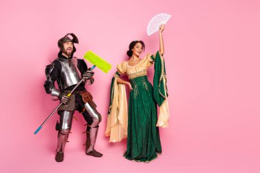 Playful image of a couple in medieval costumes. The knight and princess pose humorously against a bright pink background, highlighting fashion, history, and fun within a theatrical setting. clipart