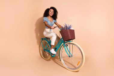 Full length photo of excited lovely girl wear blue top cycling empty space isolated beige color background. clipart