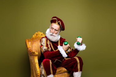 Depicting a mature man in full Renaissance attire, seated against a khaki-colored background, displaying an amusing juxtaposition of vintage glamour and contemporary exercise. clipart