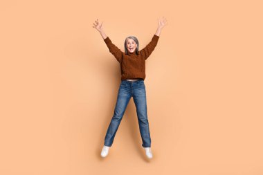 Senior woman leaps joyfully wearing casual outfit, showing excitement and vitality in a professional photo with beige as the primary color. clipart