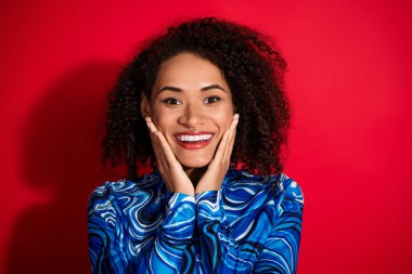 Beautiful young woman with curly hair, dressed in stylish blue attire, smiling and expressing joy, with a solid red background enhancing the vibrant colors of the setting. clipart