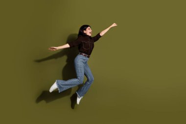 Young adult woman in a casual, elegant outfit, playfully jumping before a khaki green backdrop. Captivating moment of happiness, charm, and expression, symbolizing stylish, energetic, and optimistic clipart