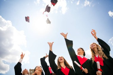 Happy young graduates celebrating their university achievements outdoors, throwing caps in the air, capturing the euphoric moment under the sunny urban sky. clipart