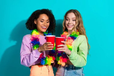 Two cheerful women holding red cups, adorned with leis, enjoying a festive moment on a teal backdrop. Represents friendship, happiness, and celebration. clipart