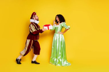 An aristocratic man offers a present to a delighted woman dressed elegantly against a vibrant yellow background, emphasizing joy and playful historical cosplay. clipart