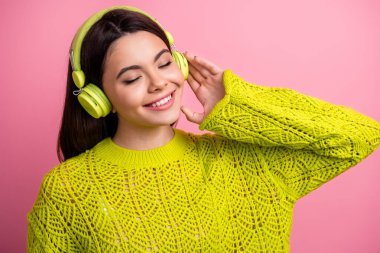 A stylish young woman wearing yellow knitwear and headphones smiles while enjoying music against a pink background, embracing happiness, fashion, and modern technology in a vibrant and trendy clipart