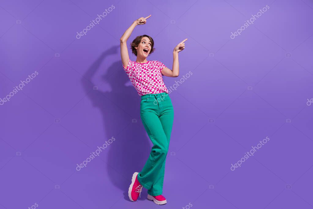 Full body photo of attractive young woman point excited empty space dressed stylish pink clothes isolated on violet color background.