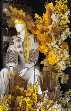 Ukrayna ulusal kostümlü bir kız manken sarı çiçeklerin arka planına karşı. Lviv 'deki hediyelik eşya dükkanı.