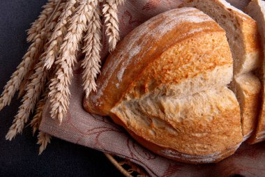 Koyu arkaplanda buğday kulaklı taze pişmiş ekmek. Dilimlenmiş ekmek