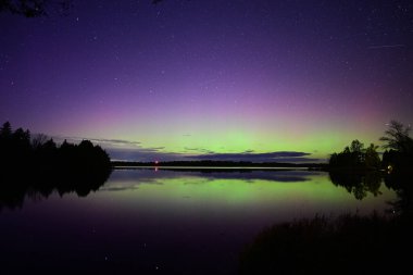 Kuzey Işıkları ya da Aurora Borielis dinamik yeşil ve pembe renkleri bir gölün üzerinde parlayan gökkuşağını gösteriyor