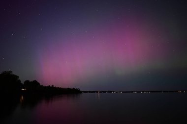 Kuzey Işıkları ya da Aurora Borielis dinamik pembe renkleri gösteren bir gölün üzerinde parlayan gökkuşağı