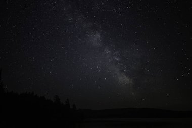 Sükûnet dolu bir yıldızın gece sahnesi ve durgun bir tatlı su gölünün üzerinde hafif bir Samanyolu parıltısı.