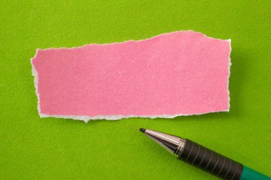 Blank paper with pen on green background. Top view of pink paper piece with copy space.