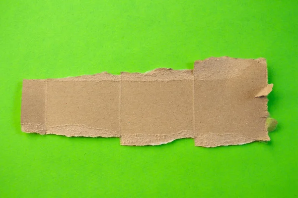 Ripped cardboard paper on a green background. Torn paper piece.