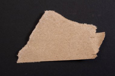 Ripped cardboard paper on black background. Torn paper piece.
