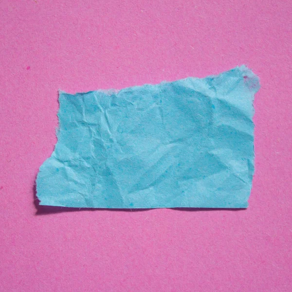 Crumpled blue paper piece on a pink background. Torn paper background.