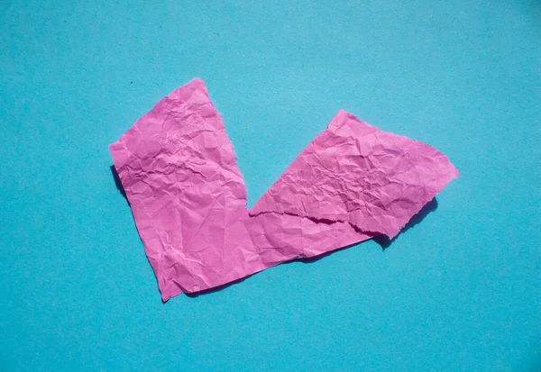 Crumpled pink paper piece on a blue background. Torn paper background.
