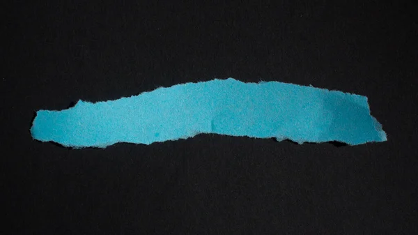 Blue torn paper piece isolated on a black background. Ripped blank paper with copy space for text.