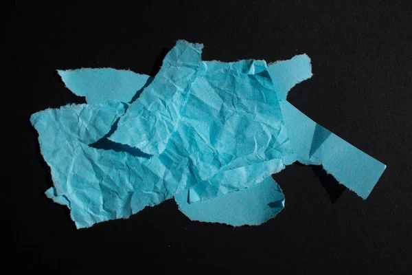 Blue torn paper piece isolated on a black background. Ripped blank paper with copy space for text.