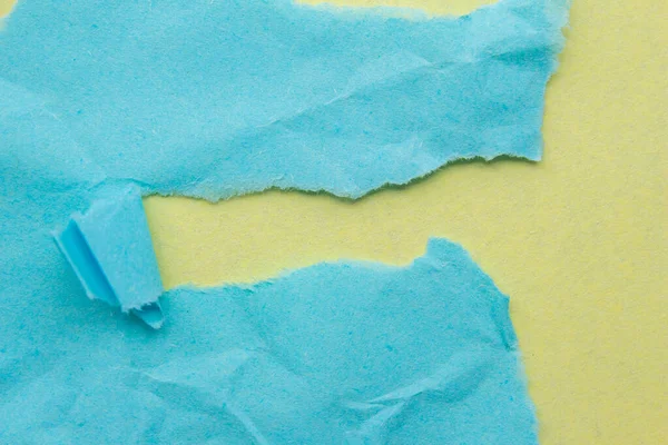 Creased blue paper piece on a yellow background. Crumpled torn paper edge texture background.