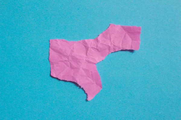 Crumpled pink paper piece on a blue background. Torn paper background with copy space for text. Wrinkled texture.
