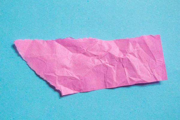 Crumpled pink paper piece on a blue background. Torn paper background with copy space for text. Wrinkled texture.
