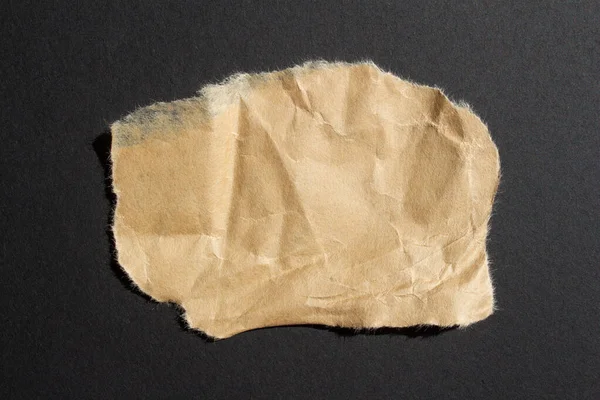 Crumpled brown paper on a black background. Ripped paper background.