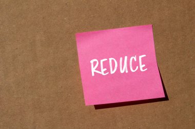 Kahverengi arka planlı pembe kağıt etiketine yazılan kelimeyi küçült. Kavramsal küçültme sembolü. Boşluğu kopyala.