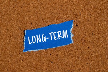 Kahverengi arkaplanlı mavi kağıt parçasına yazılmış uzun vadeli kelimeler. Kavramsal uzun dönem sembolü. Boşluğu kopyala.