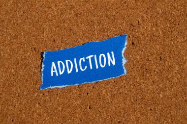 Kahverengi arkaplanlı mavi kağıt parçasına yazılmış bağımlılık kelimesi. Kavramsal bağımlılık sembolü. Boşluğu kopyala.