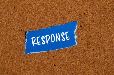 Kahverengi arkaplanlı, yırtık mavi kağıt parçasına yazılmış bir yanıt. Kavramsal tepki sembolü. Boşluğu kopyala.